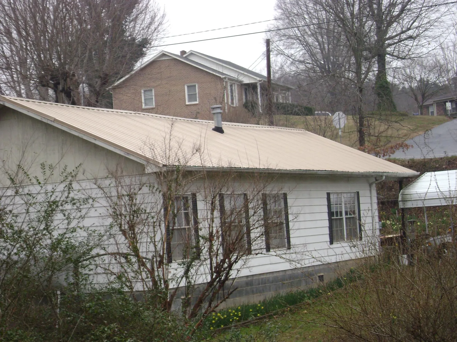 Tan metal roof on a white sided house set into a hillside — Commercial Roofing by Roofing Brothers in Ararat